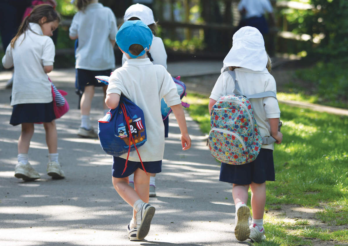 Children in white t-shirts and their backpacks walking on a summer day